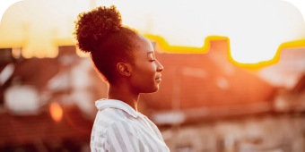 Woman standing outdoors with the sun setting besides her. 
